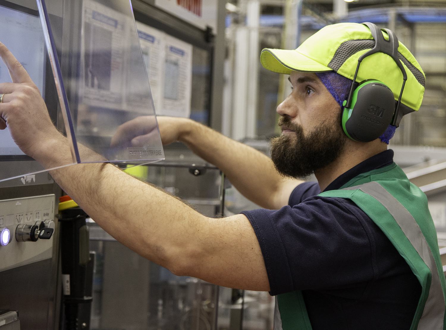 Machine operator in ear defenders at a control panel