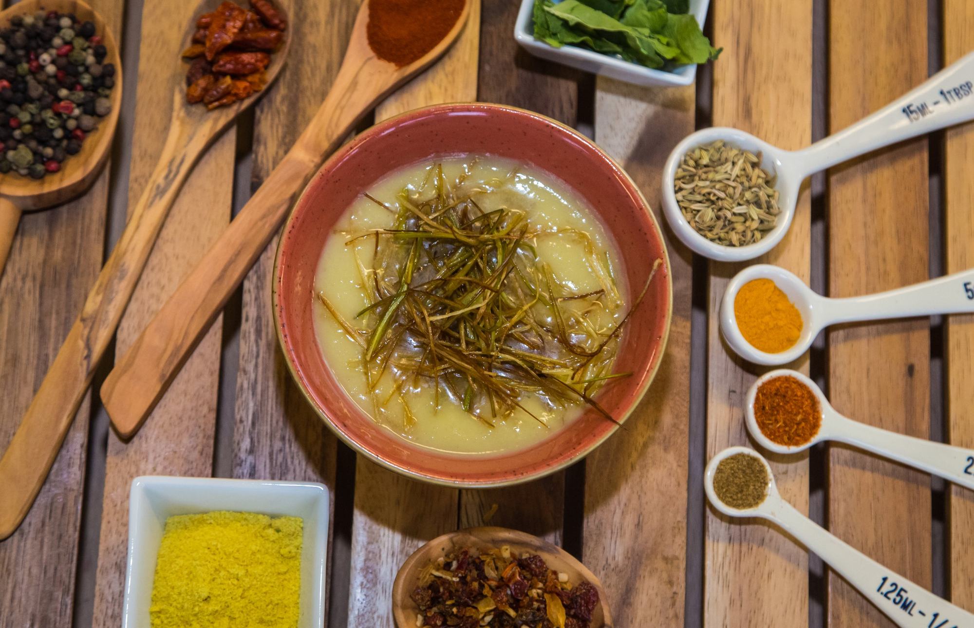 Overhead soup bowl surrounded by spice spoons