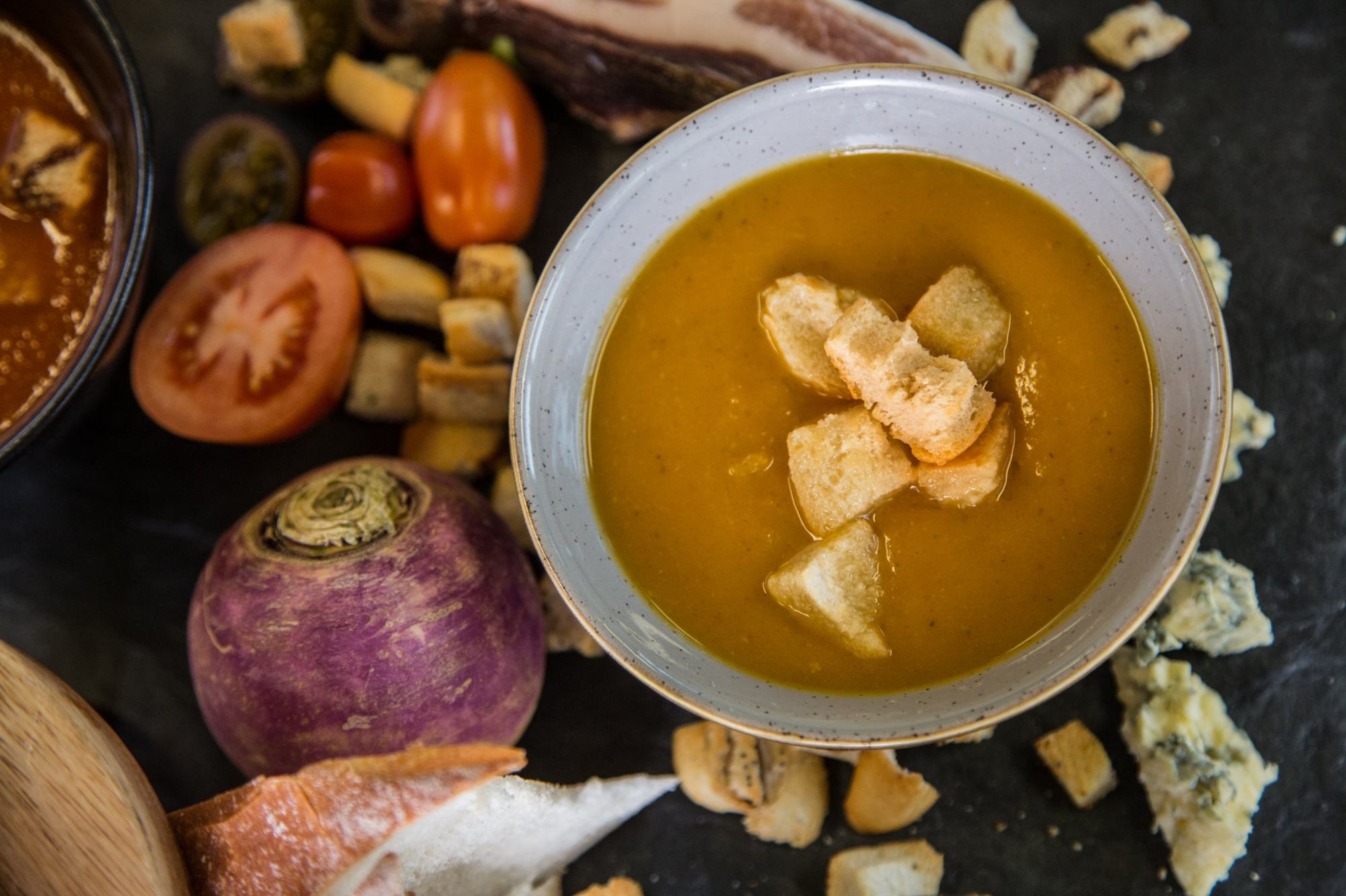Bowl of soup with croutons styled with fresh ingredients on slate