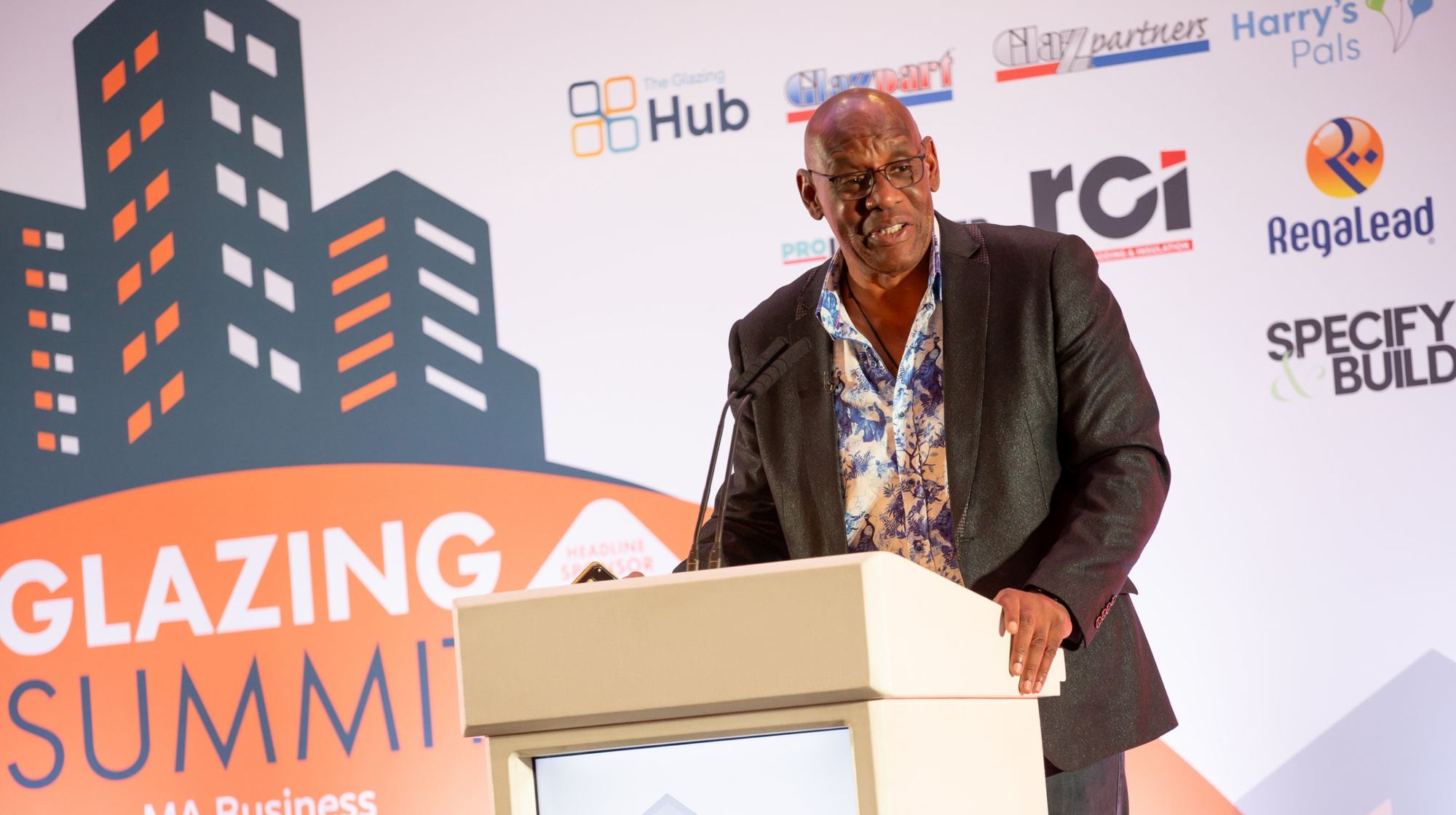 Speaker at the lectern with sponsor logos behind at the Glazing Summit