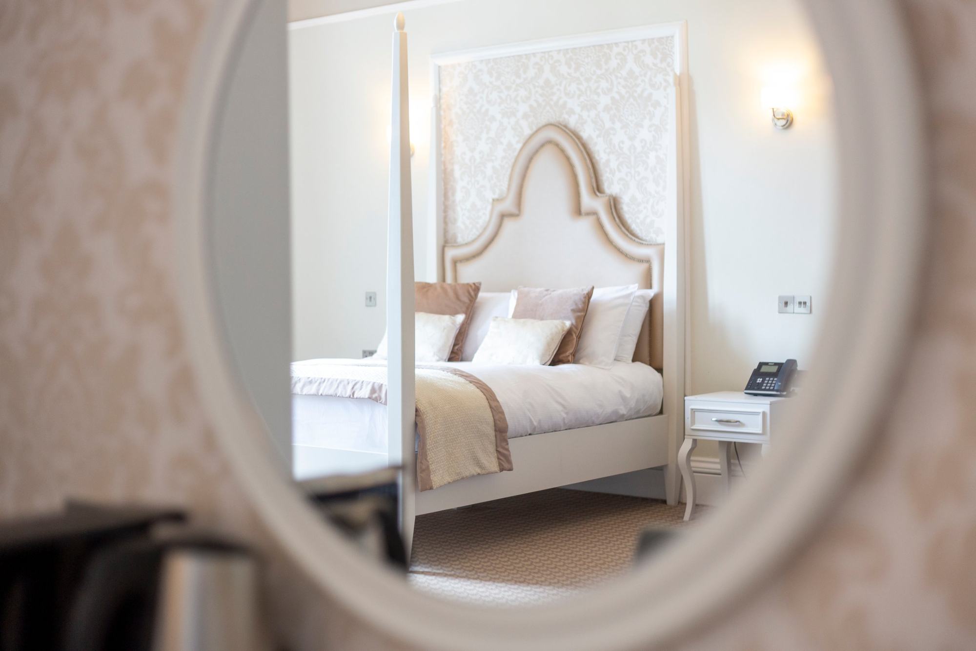 Four-poster hotel bed seen through an oval mirror