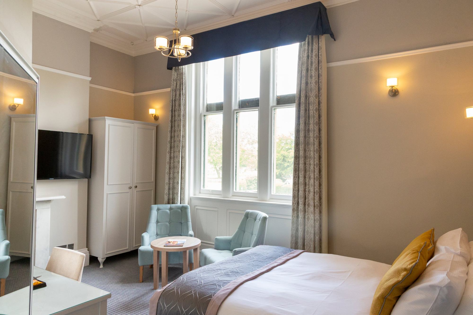 Bright hotel bedroom with tall sash windows and armchairs