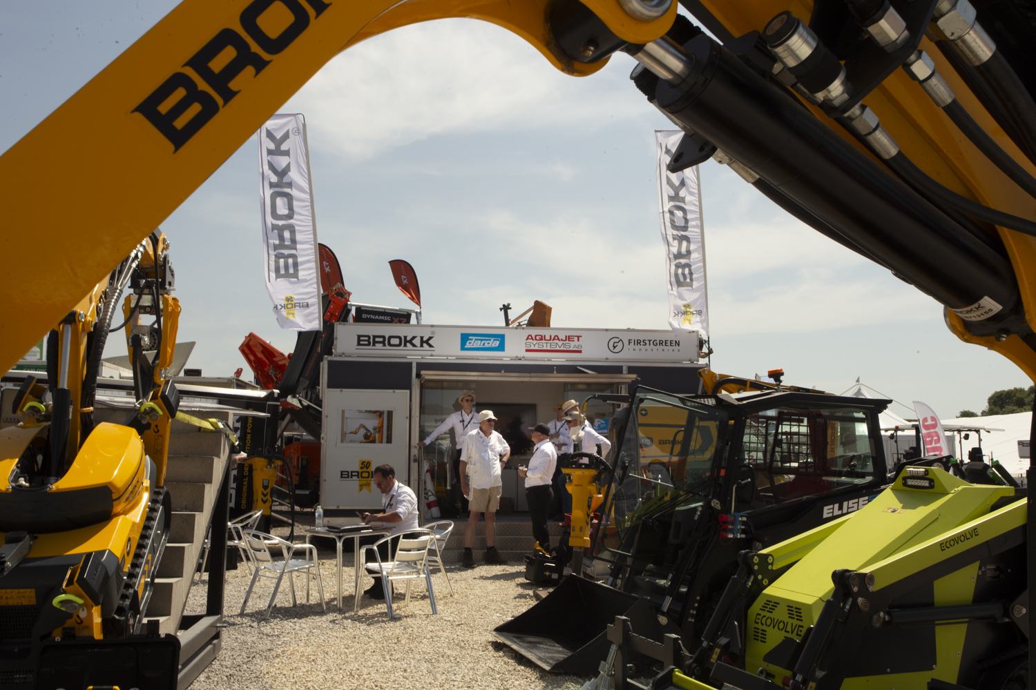Exhibitors on a stand framed by machinery at an outdoor trade show